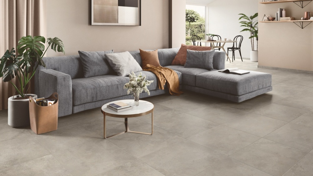 Vardagsrum med grå plattor i 60x60 cm på golvet. I bild syns också en mörkgrå soffa med kuddar och ett soffbord